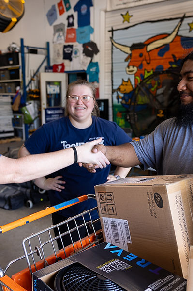 Woman in blue shirt shakes man's hand over boxes in warehouse.