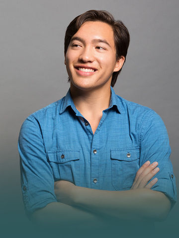 Young man in blue shirt smiling, arms crossed, looking right confidently.