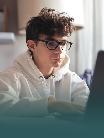 Young man in glasses focused intently on laptop, wearing white hoodie.