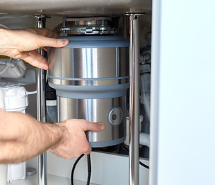 Plumber inspecting garbage disposal unit under kitchen sink for clogs or damage