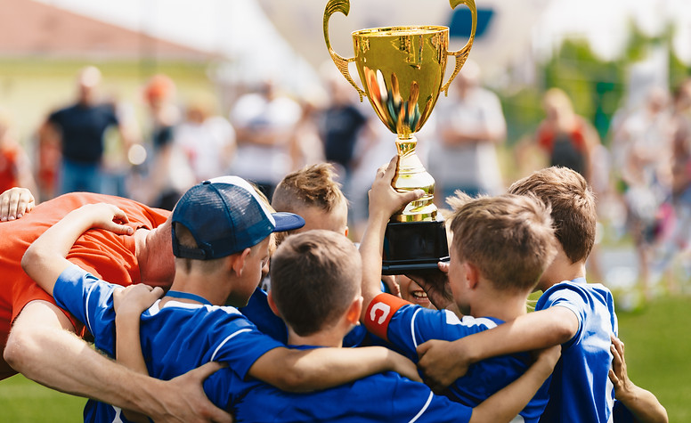 Boys sport team celebrating success with young coach. Team captain rising golden trophy wi