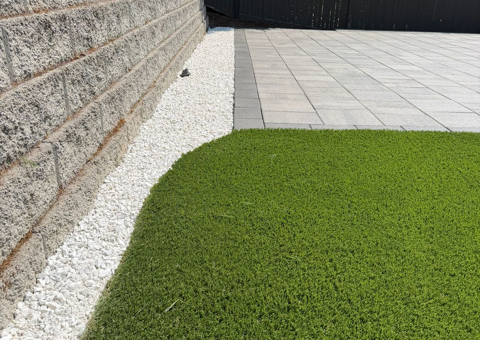 Artificial grass lawn next to white gravel and stone wall