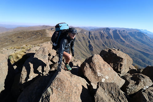 Female athlete scrambling over rocks to the summit of a mountain.