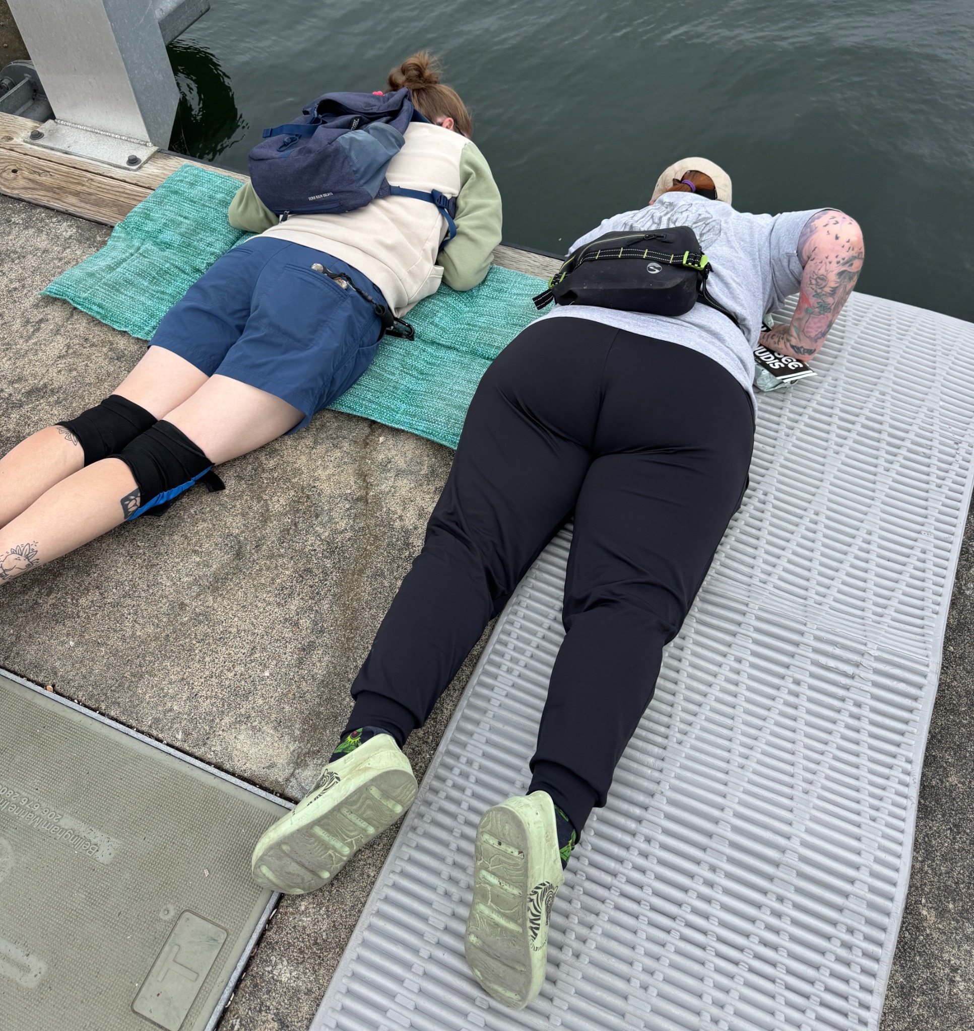 Two people lying face-down on a floating dock looking into the water