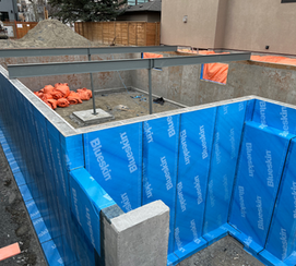 Custom home basement walls with continuous Blueskin waterproofing membrane installed prior to backfilling, highlighting premium foundation detailing.