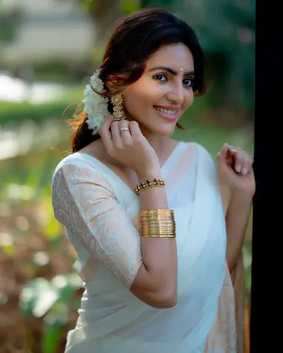 Athulya Ravi in jacquard kasavu white saree with designer blouse, jasmine flowers, golden bangles, and jimikki earrings, showcasing traditional Kerala attire.