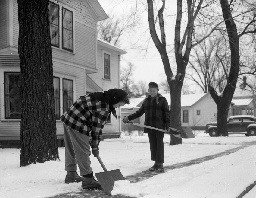 Photo from the Stevens Point Journal. Caption from 11/28/1949. The first snow that stayed on the ground this season brought both work and play for Stevens Point young people. In upper picture, Sally Benson, 1001 Main street, is shown in front of her home when Jimmy Marko, 1310 Clark street, came along.