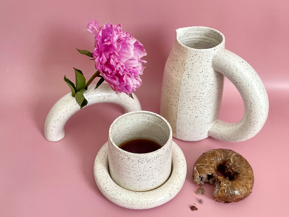A handmade ceramic pitcher, cup and saucer and a half donut vase