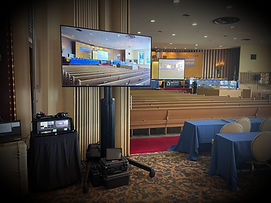 A large projection sreeen with a projector for the pressburger sanctuary in the teaneck jewish center in teaneck nj.  an additional LED monitor on a floor stand next to a rack of audio and video equipment