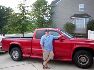 Zach stands next to a red truck he bought himself.