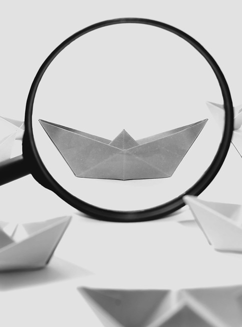 Orange paper boat under magnifier among of a group of green paper boats on white backgroun