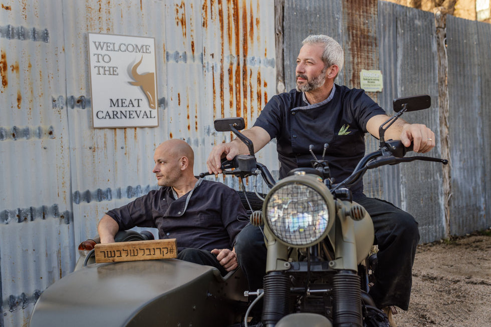 two men sit on a motorcycle in front of a sign that says welcome to the meat carnaval