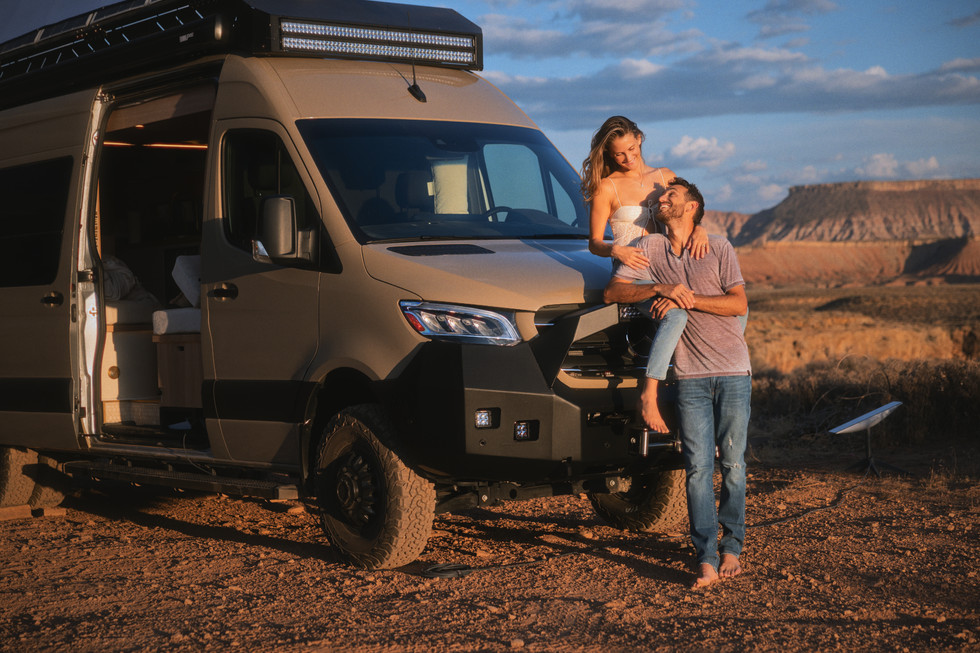 a man holds a woman on his shoulders in front of a van