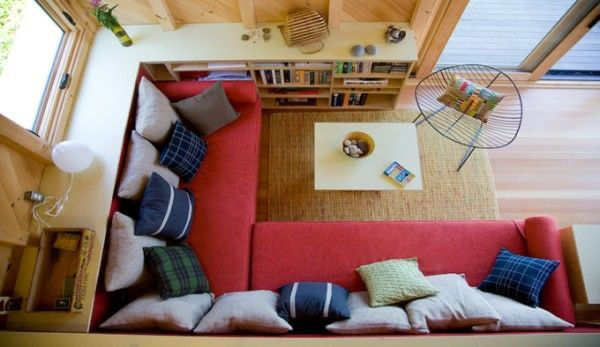 Cozy living room with red sectional sofa, colorful pillows, and a square coffee table on a beige rug. Built-in bookshelves and wood decor abound.