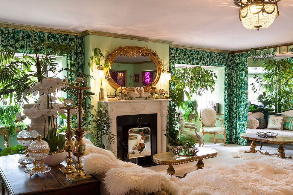 The Green Room lounge at The Pink House Essex, Eaton House Studio — a lush botanical inspired living room with open fireplace, gold chandelier, tropical wallpaper and antique furnishings"