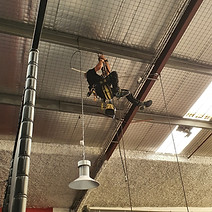 Cordiste se déplaçant sur une structure métallique au dessus d'un trampoline pour ré-accrocher une suspension luminaire