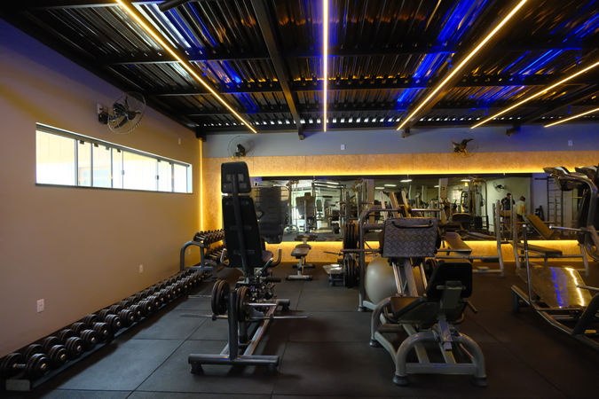 Área de musculação da Academia Madalozzo Fitness em Curitiba com iluminação linear em LED e espelho panorâmico.