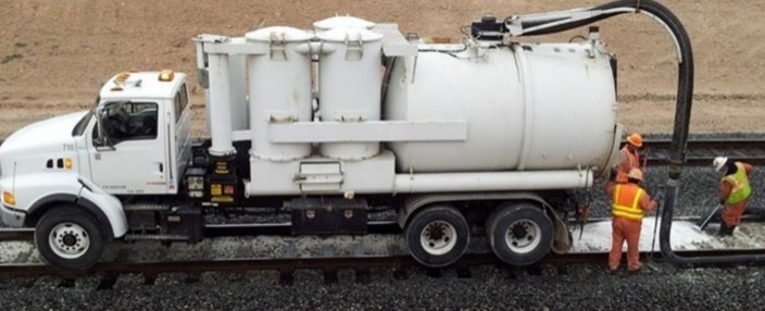 Vacuum truck at work on a rail bed, its boom hose reaching down to the ground