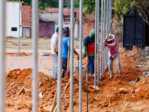 Trabalhadores executam as obras do novo Complexo Esportivo de Taquaruçu, ao lado do ginásio poliesportivo. Máquinas e operários atuam na preparação da base do campo de futebol society e da quadra de areia, em área cercada por vegetação, marcando o início da construção do espaço que contará ainda com vestiários, iluminação em LED e infraestrutura de lazer.