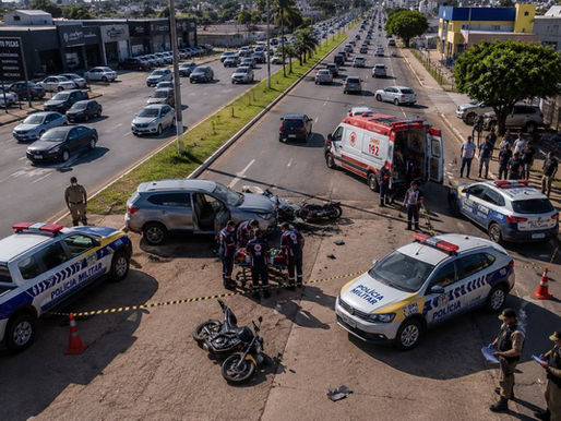 Imagem ilustrativa de um acidente de trânsito em avenida urbana, com viaturas da Polícia Militar, ambulância do SAMU, motocicleta caída e equipes de atendimento em uma via movimentada.