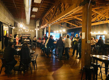 a lively dystopian state taproom with refinished floors, upcycled furniture and group of people drinking and connecting with each other