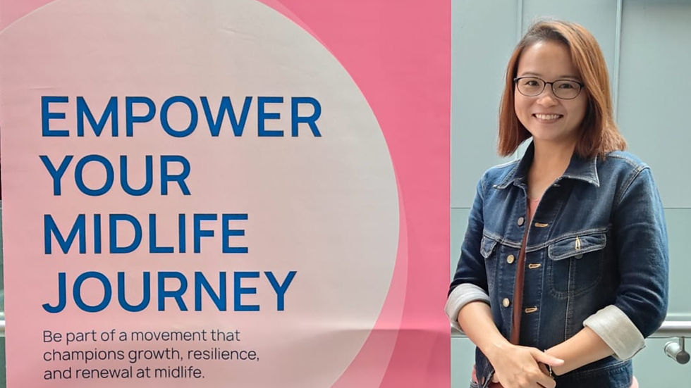 Smiling woman in a denim jacket stands by a pink sign reading "EMPOWER YOUR MIDLIFE JOURNEY" with a message about growth and renewal.