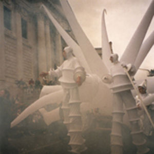 inflatable white spiky shape behind two stilt walkers emerging from the mist