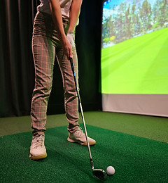 Indoor golfing practice session with a virtual simulator on a green turf surface.jpg