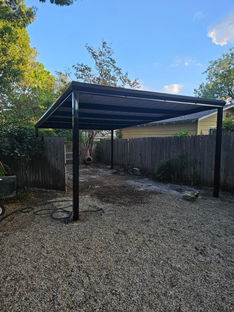 Open black metal carport in Waco, Texas, with a modern steel roof supported by durable steel framing, located next to a concrete driveway.