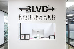 BLVD Estate, inside of their offices. A white wall with BLVD logo and the receptionist desk beneath