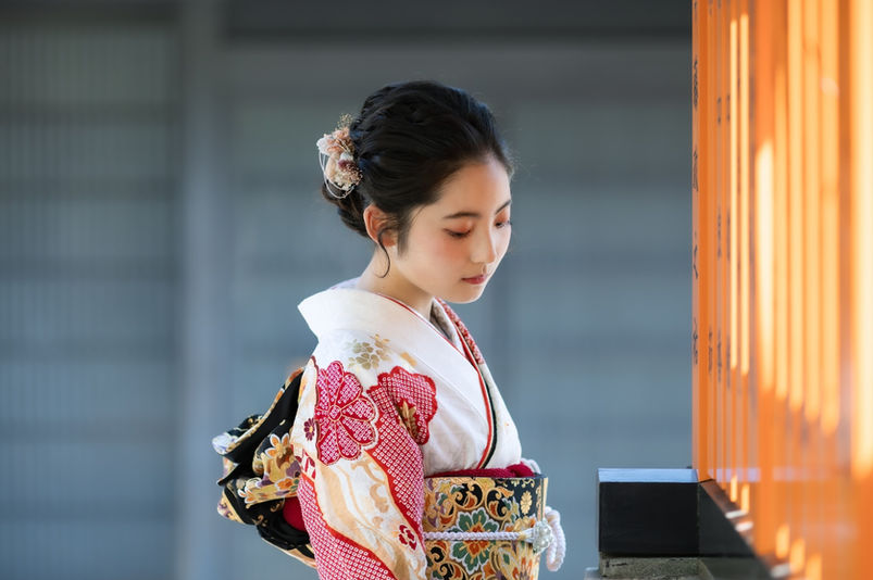 朱色の玉垣を背景にした振袖姿の女性の横顔
