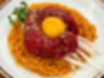 Raw beef with sesame seeds and egg yolk on top of spicy noodles, garnished with sprouts and thin white radish slices on a plate.