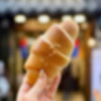 Hand holding a golden-brown salted bread in focus, with a blurred store background, conveying a cozy atmosphere.