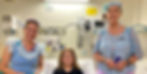 Young girl smiles with two fairy volunteers in hospital room.