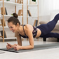 Fit woman doing yoga plank and watching online tutorials on laptop, training in living roo