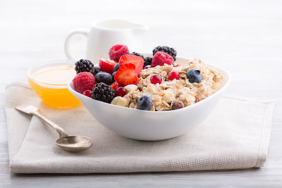 Bowl of oatmeal topped with berries on a napkin, with honey, spoon, and white mug in a bright breakfast setting