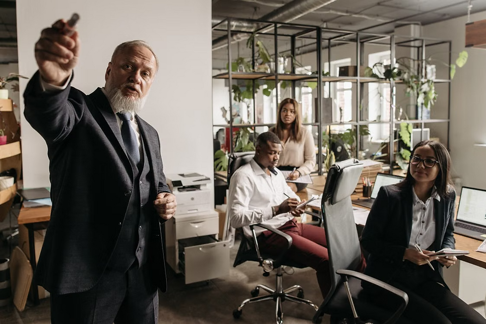 Image via https://www.pexels.com/photo/a-man-in-black-suit-talking-beside-people-in-the-office-7654410/