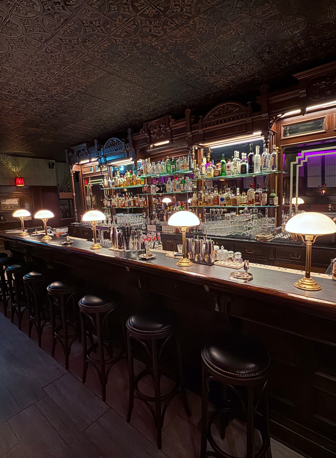 The curated spirits shelf and bar stools at Twent's under warm lamplight