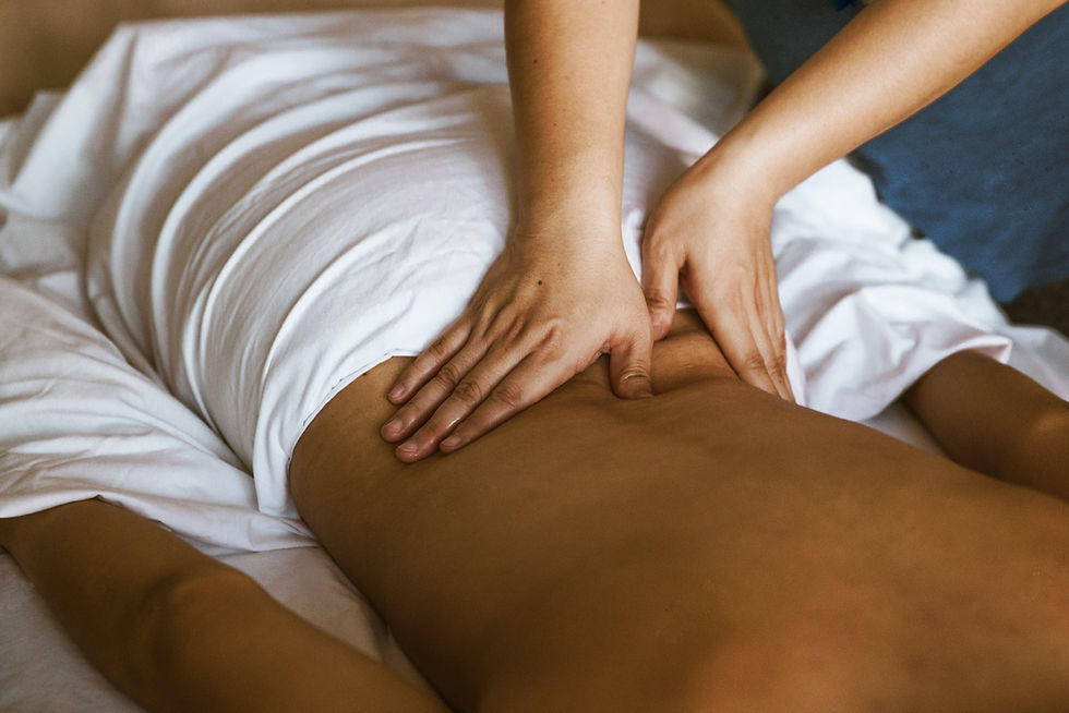 Person receiving a massage on a white bed, hands applying pressure on the lower back, creating a calm and soothing atmosphere. Luxe Thai Massage in San Antonio