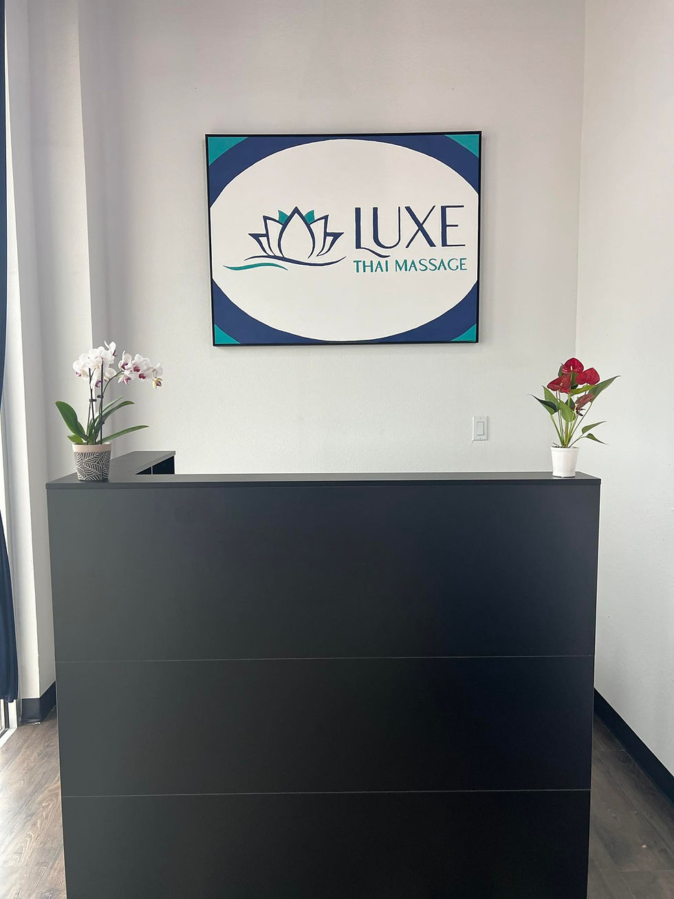 Reception desk with orchid plants and a sign reading "Luxe Thai Massage" on the wall. Minimalist decor in neutral tones. Luxe Thai Massage in San Antonio.