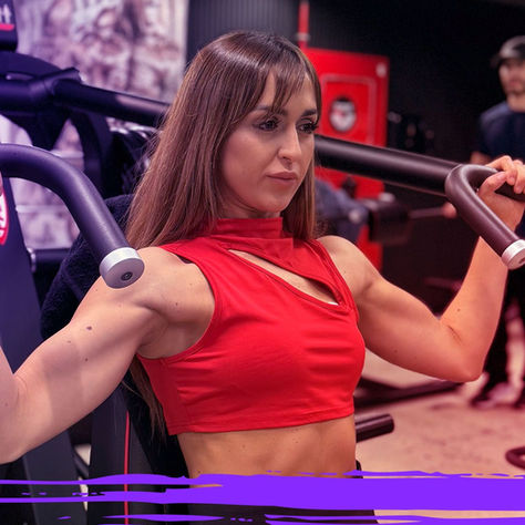 Woman performing a shoulder press exercise on a resistance machine at a gym, focusing on upper-body strength training.