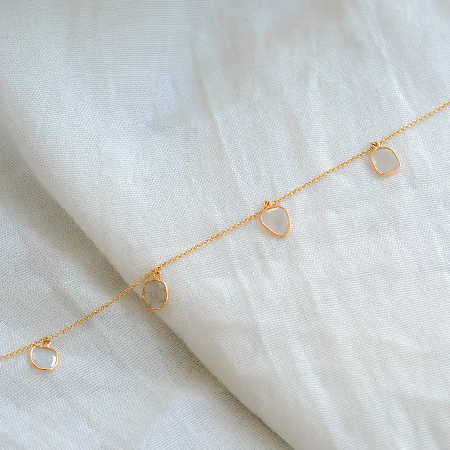 Minimal diamond charm bracelet in 18K gold styled on soft fabric background