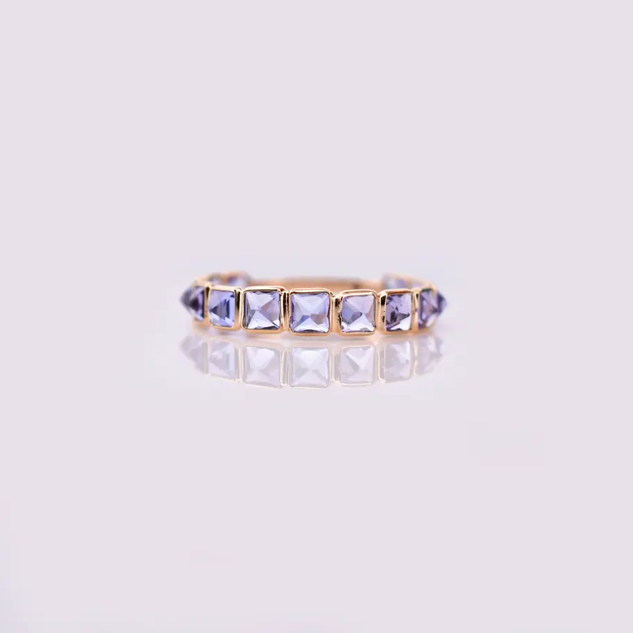 18K solid gold eternity ring with natural tanzanite gemstones displayed on a beige jewelry stand.