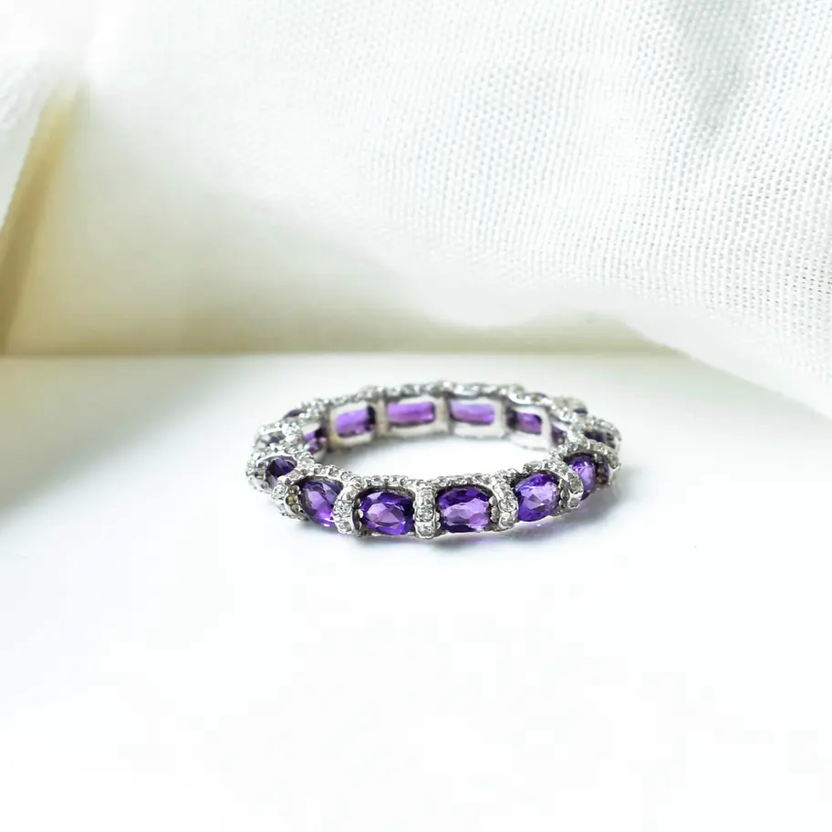 Oval amethyst eternity ring in sterling silver photographed on soft white fabric background