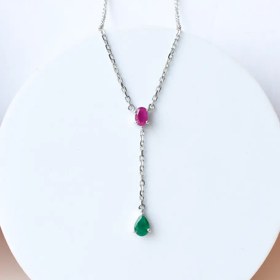 Ruby emerald necklace in sterling silver on white background Close-up of prong-set natural ruby and emerald gemstones Dainty