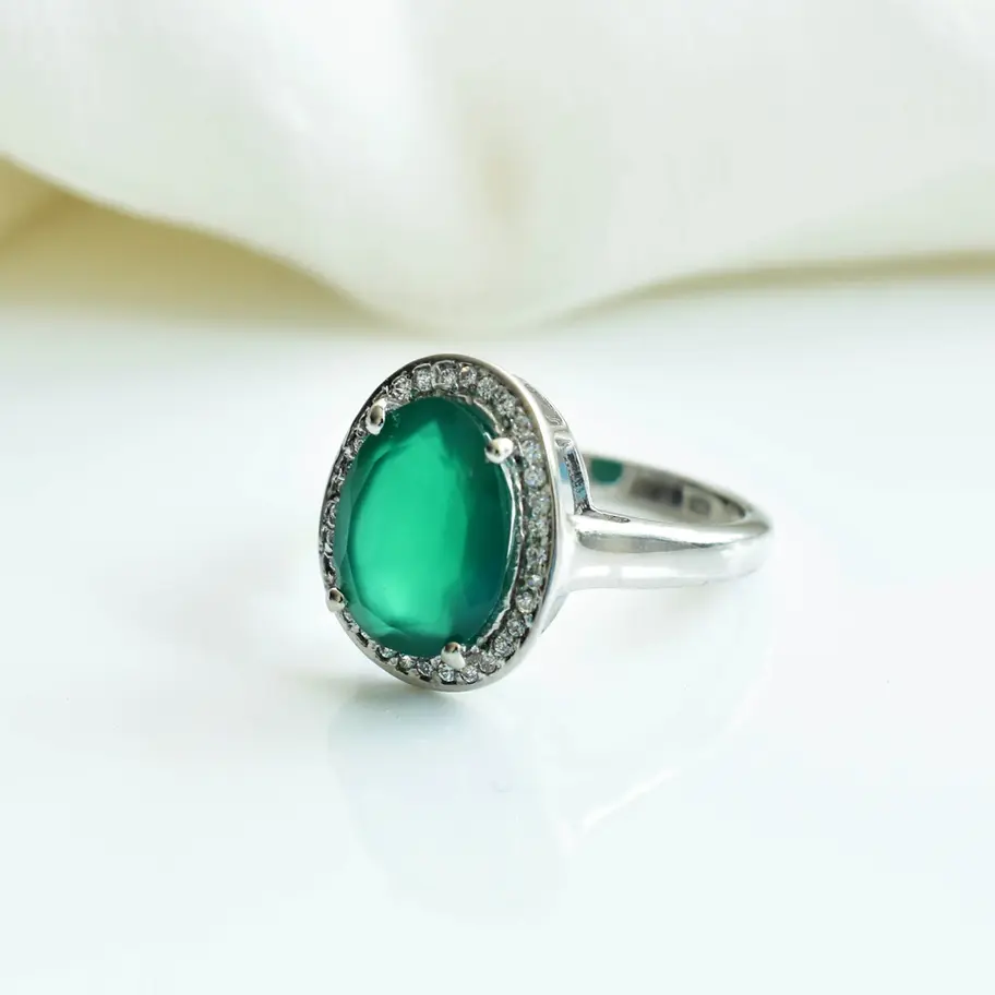 Natural green onyx oval ring in 925 sterling silver with American diamond halo setting displayed on soft white fabric backgro