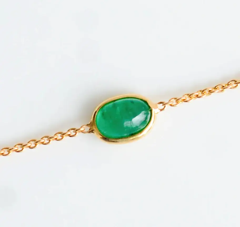 Close-up of oval green emerald stone set in 18K gold bezel style bracelet