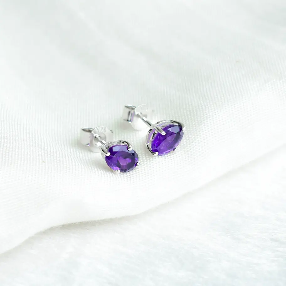 925 sterling silver oval amethyst stud earrings with vibrant purple gemstones in a four-prong setting on a soft white backgro