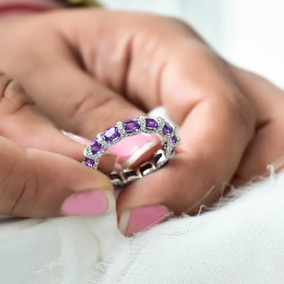 Natural amethyst eternity band ring in 925 sterling silver held between fingers, purple gemstone stackable ring