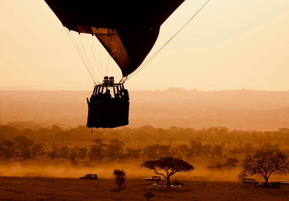 Hot air balloon flight over Tanzanian safari savannah at sunset, showcasing bespoke luxury safari experiences